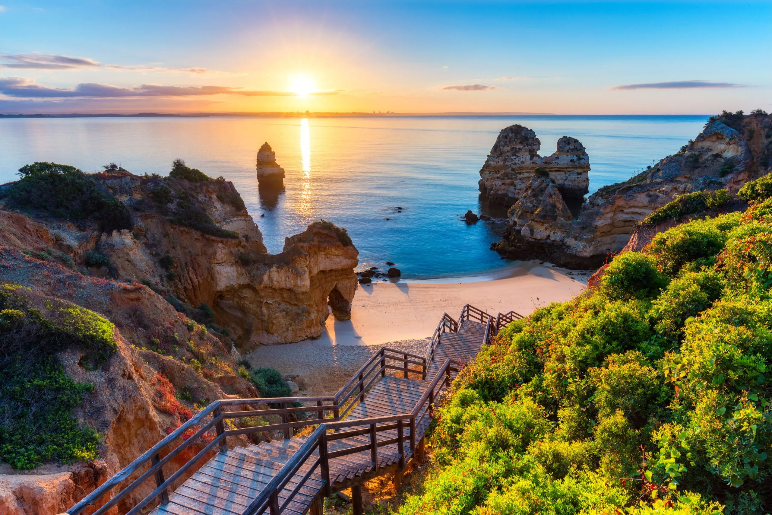 Wooden steps down to a beach and sea stacks on the Algarve coast at sunrise